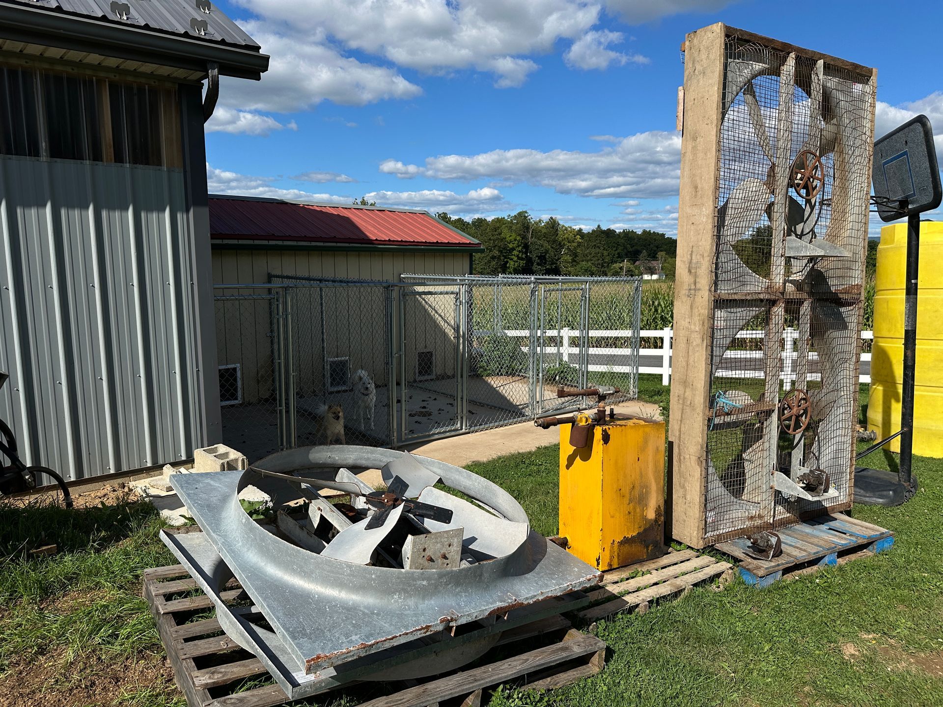 Damaged outdoor metal machinery beside a fence and building under a blue sky