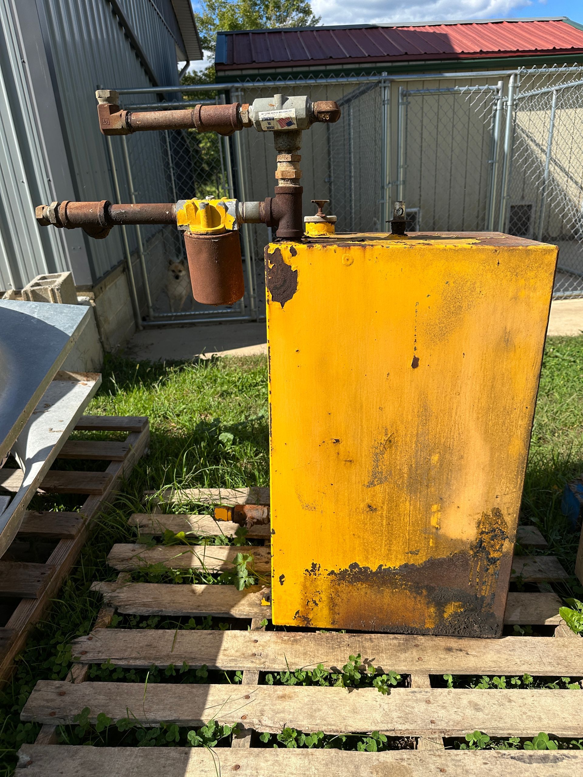 Yellow utility box with rusted pipes in a grassy yard beside a shed.