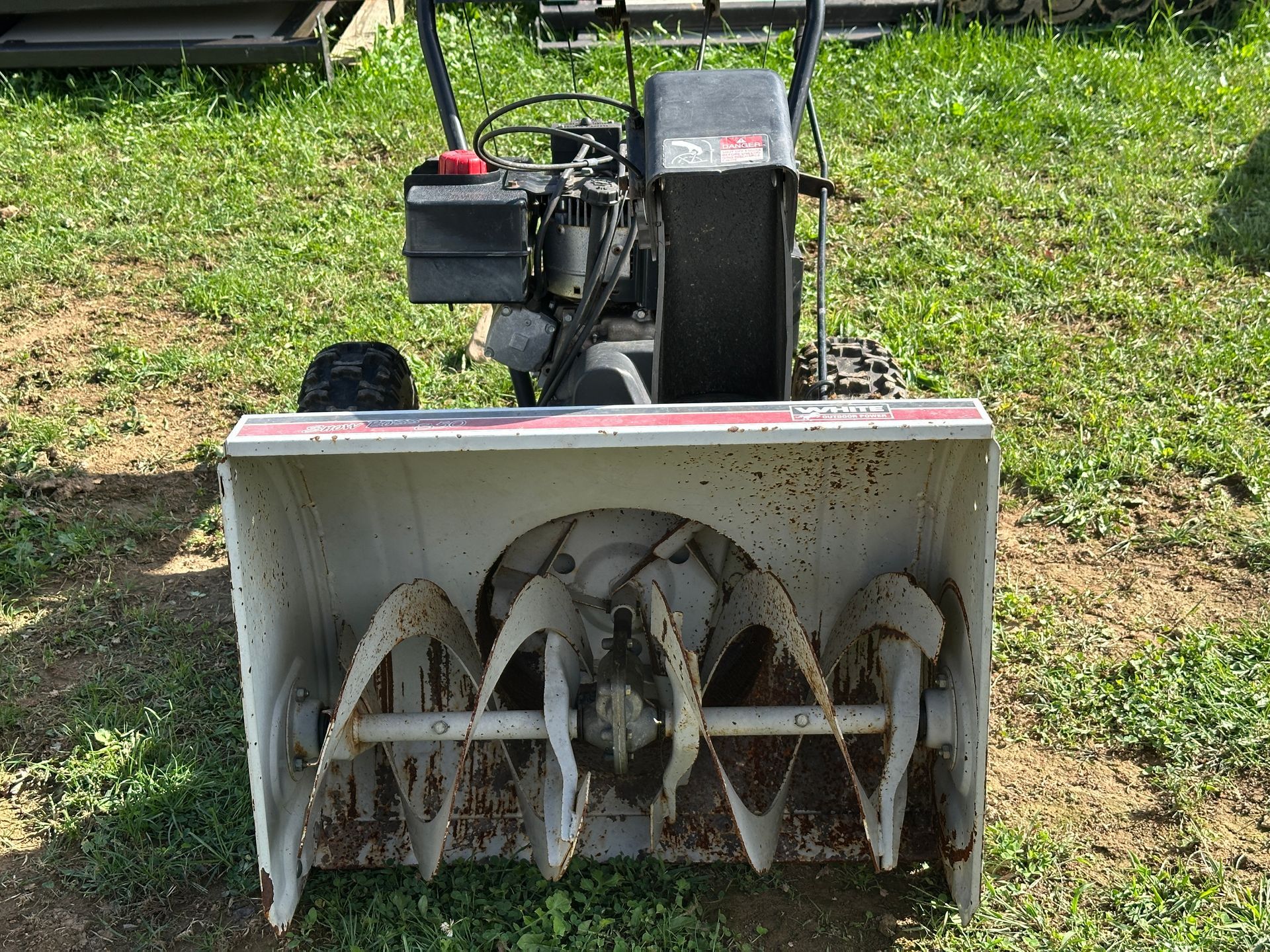 Front view of a snow blower with black engine and white auger, sitting on grass outdoors