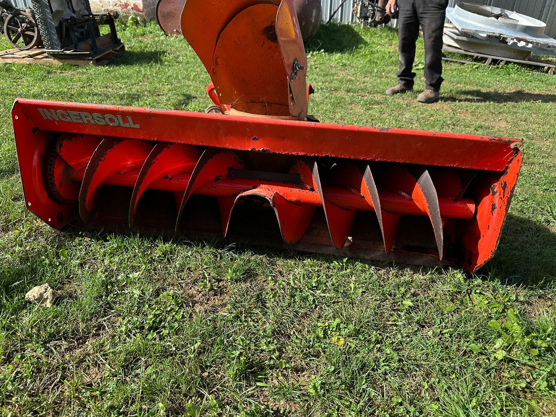 Red snowblower attachment with orange auger on grass, outdoors
