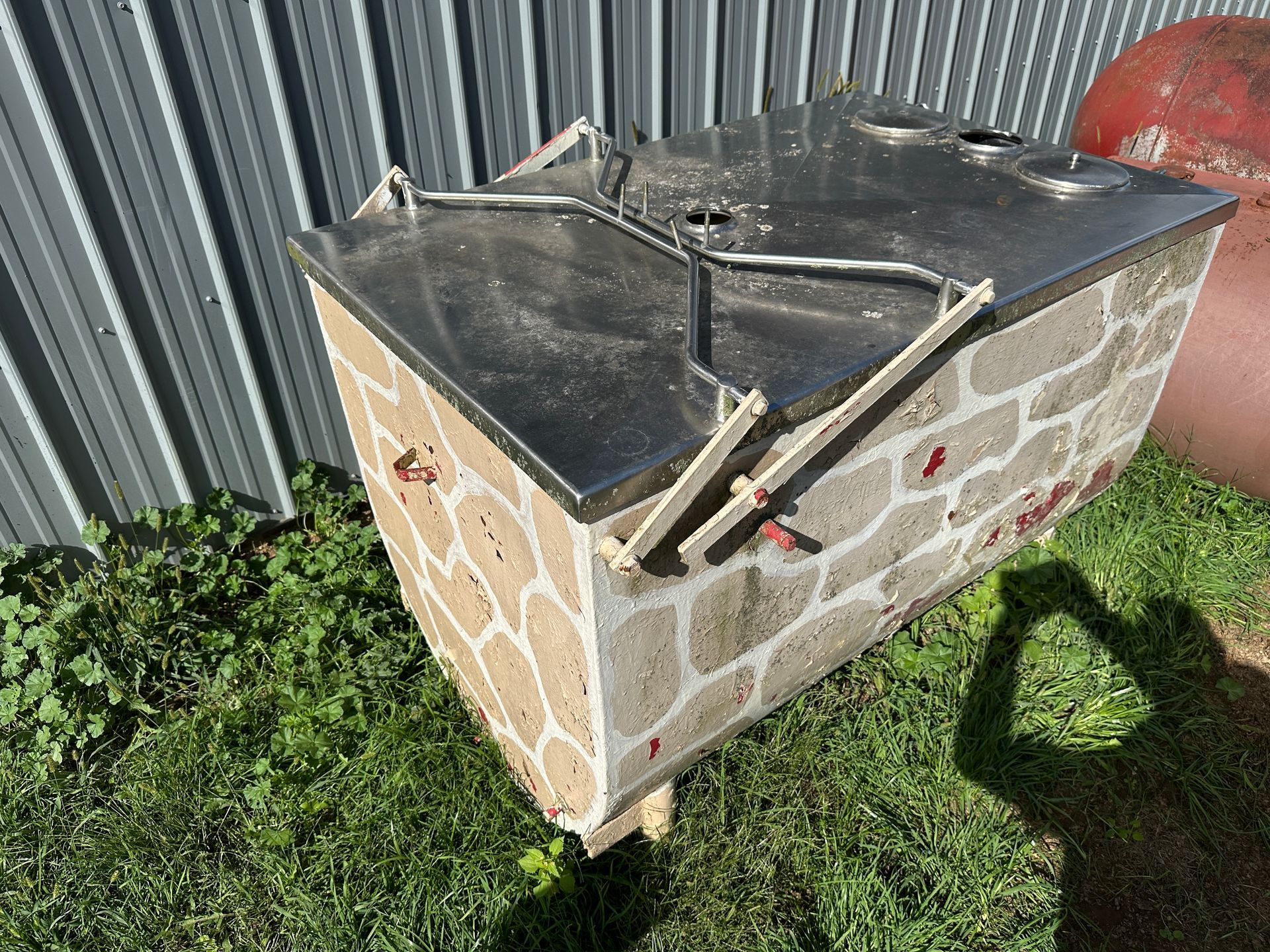 Stone outdoor box with a black tarp-covered top beside a metal fence on grass