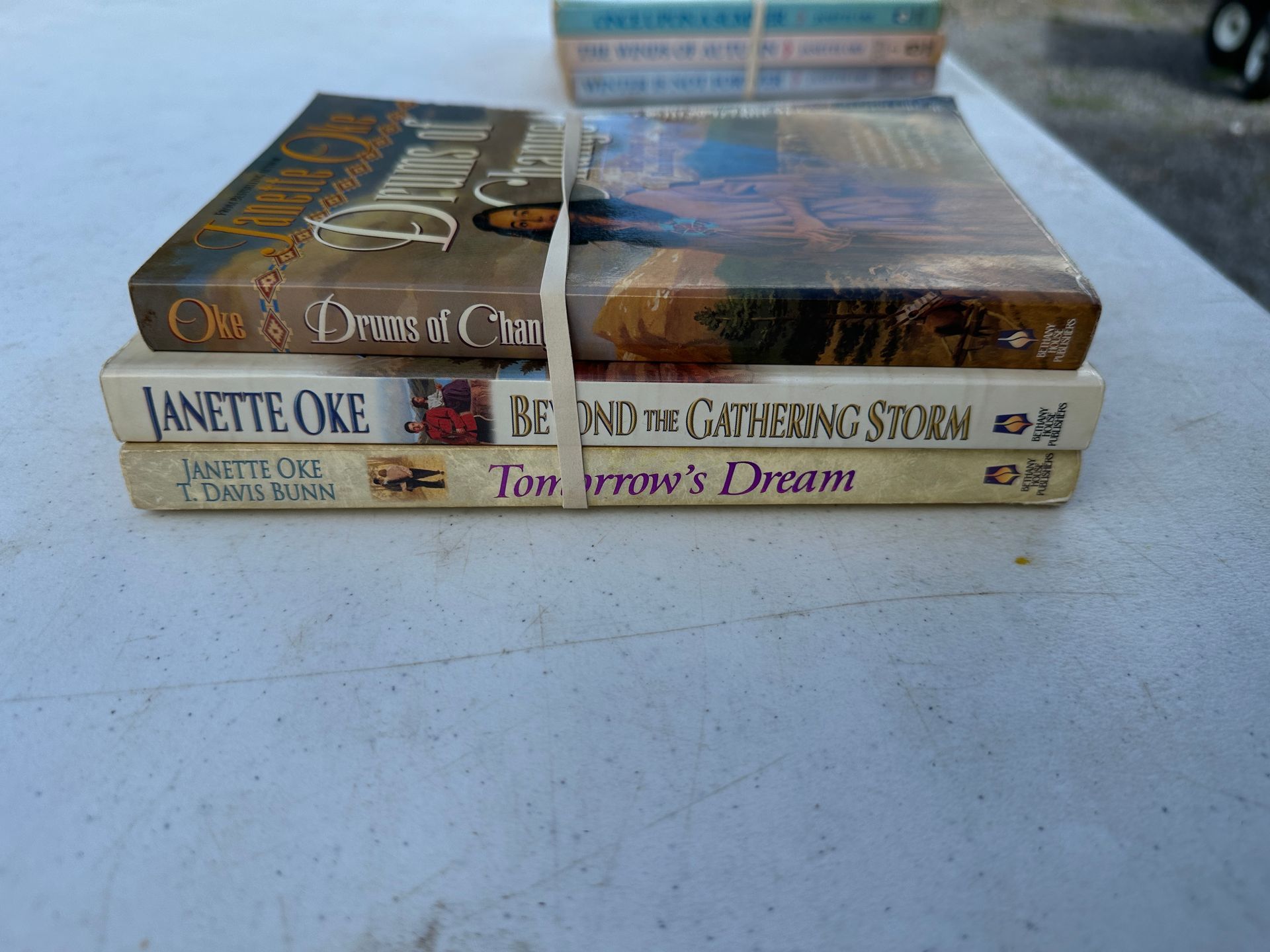 Stack of colorful paperback books on a table, with visible handwritten titles on the spines.