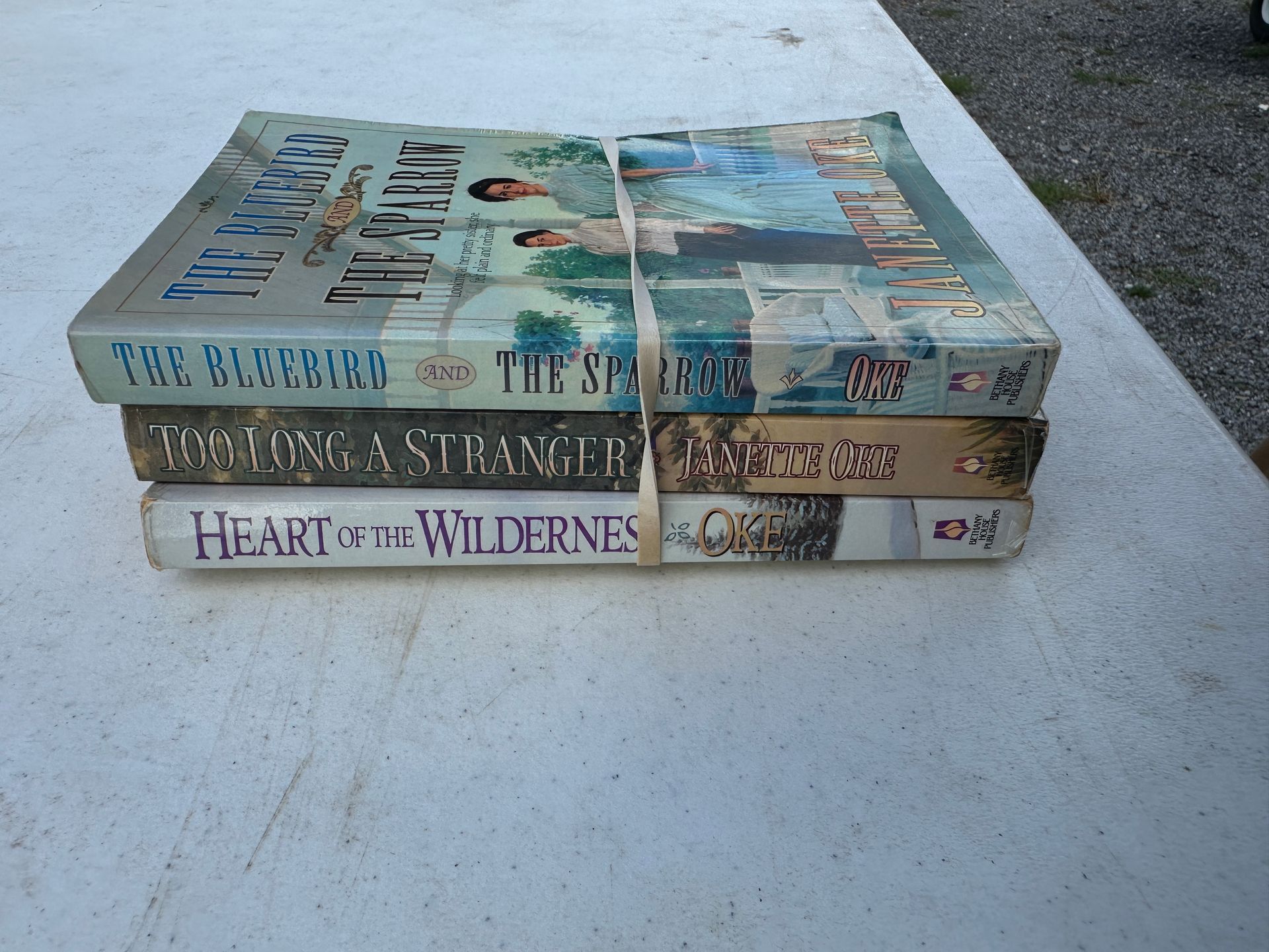 Three stacked books on a white surface outdoors, with blue and white illustrated covers.