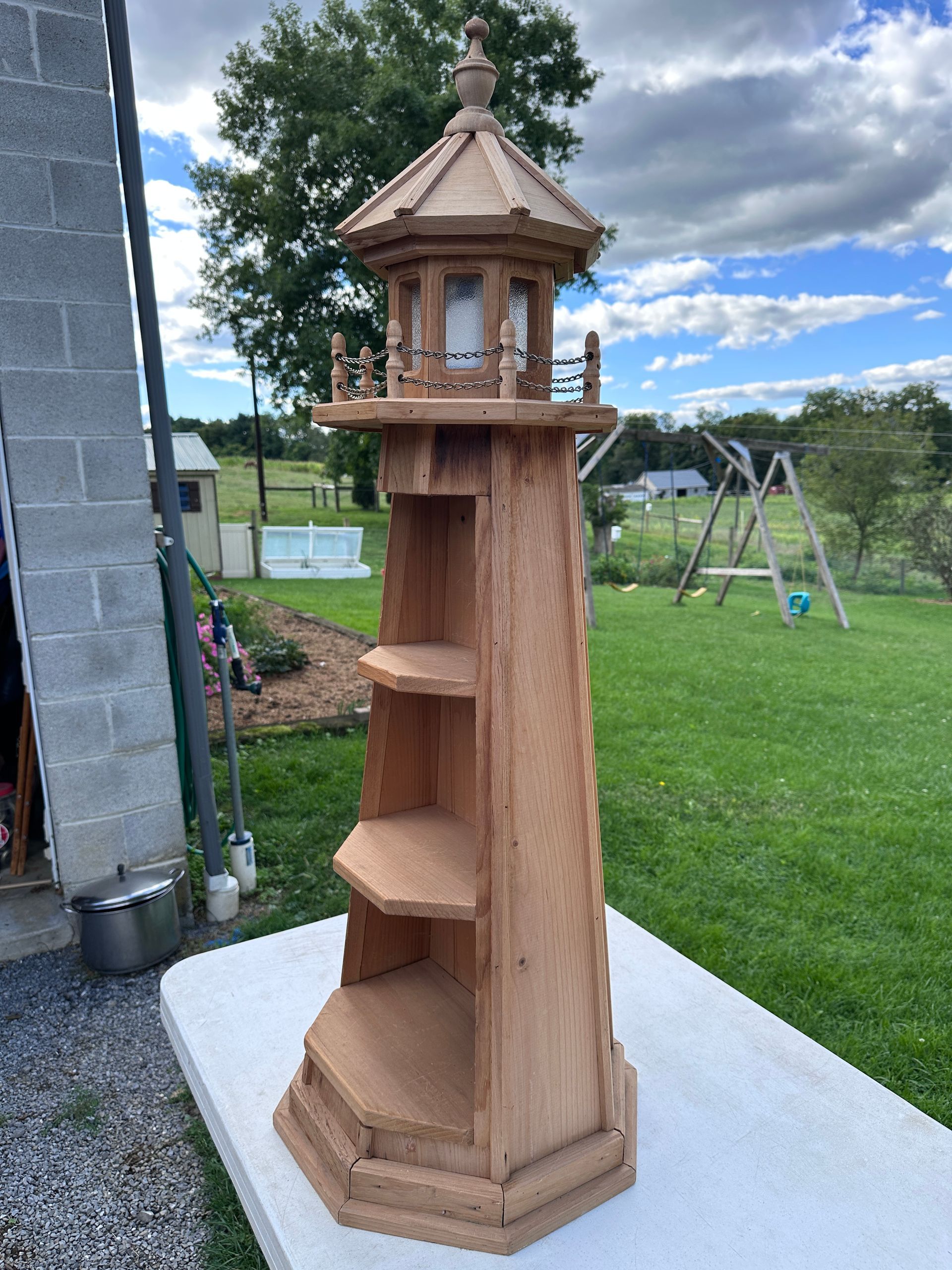 Wooden lighthouse-style birdhouse on a white table in a backyard lawn