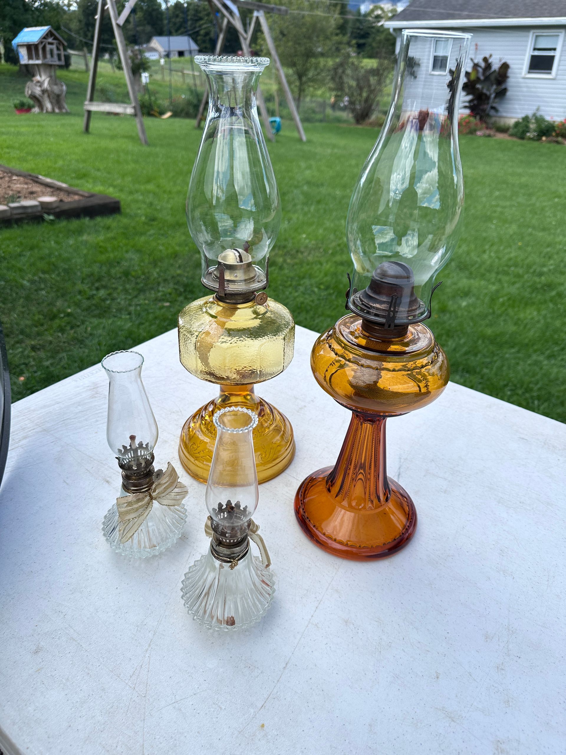 Three vintage glass oil lamps in amber, clear, and frosted glass on a white table outdoors