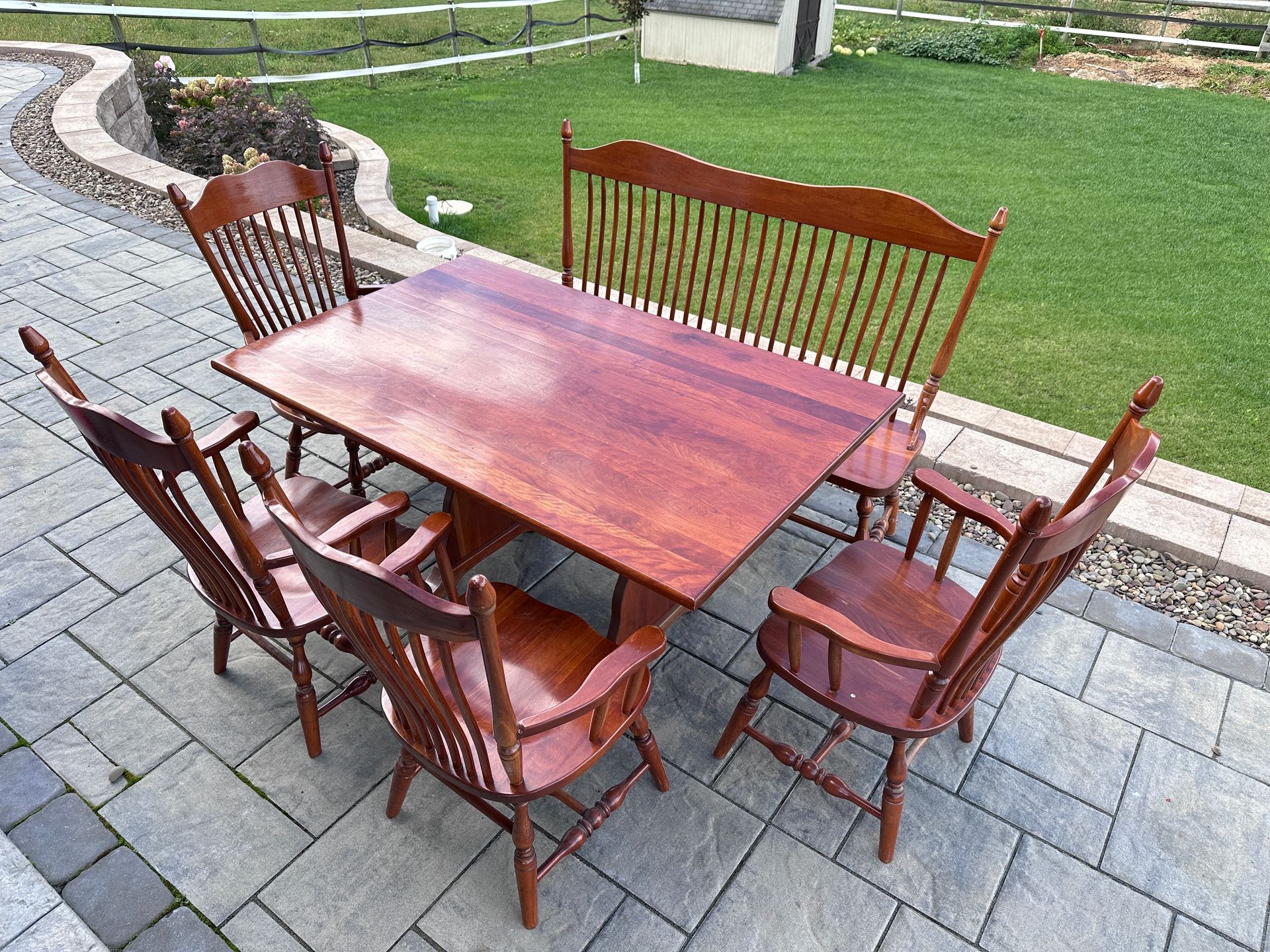 Outdoor wooden patio table with six matching chairs on a stone terrace beside a lawn