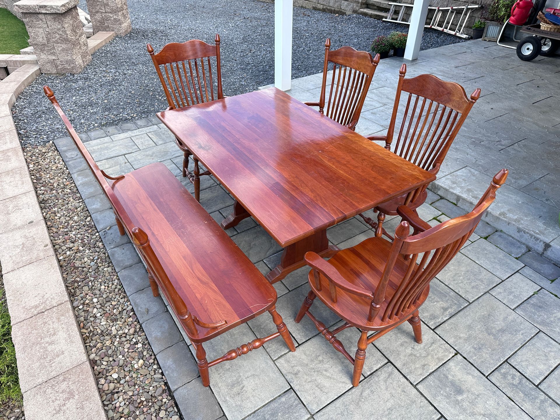 Wooden outdoor dining table with six chairs on a paved patio.