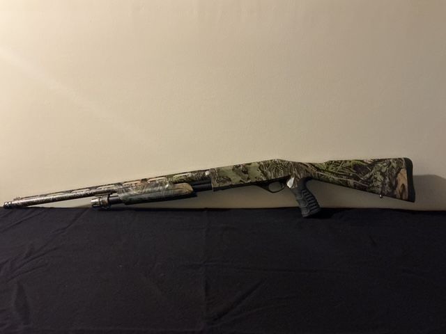 Camouflaged shotgun resting on a dark cloth surface against a light wall