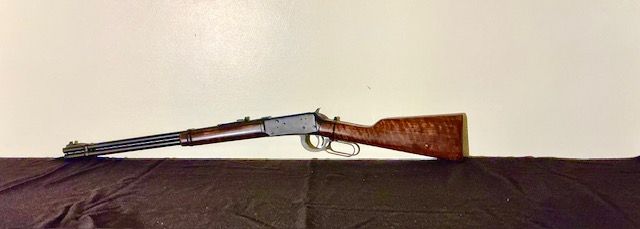 A shotgun laid horizontally on a dark surface against a light background.