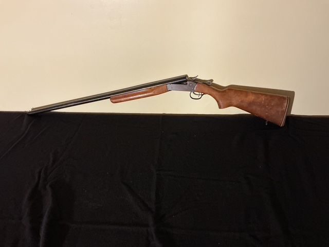 Shotgun with wooden stock and double barrels lying on a black surface against a beige background