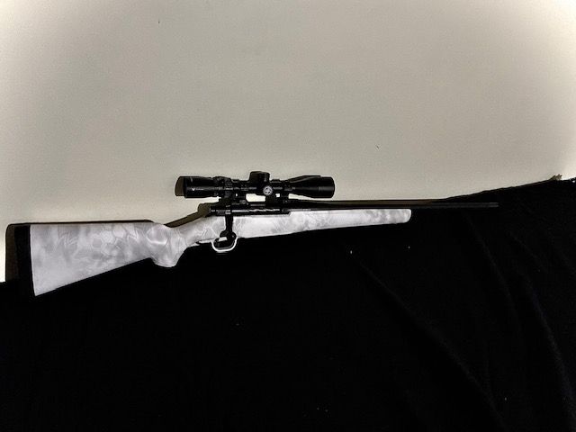 Scoped rifle on a white and black surface, viewed from the side.
