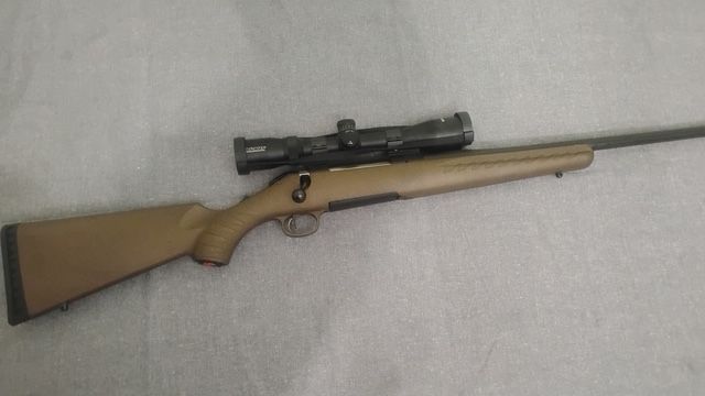Bolt-action rifle with wooden stock and mounted scope on a light gray surface