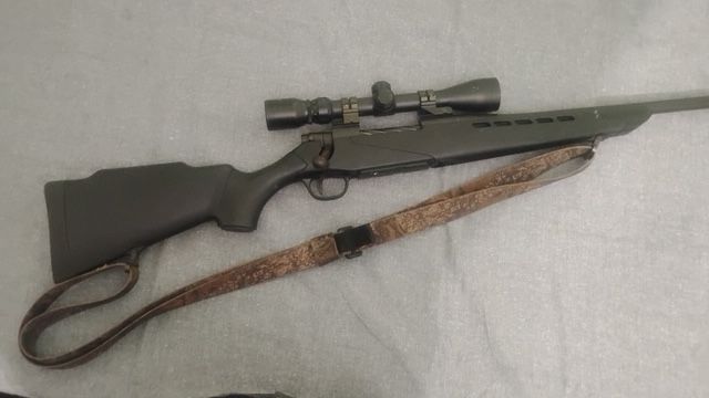 Hunting rifle with scope and camouflage sling on a light gray surface