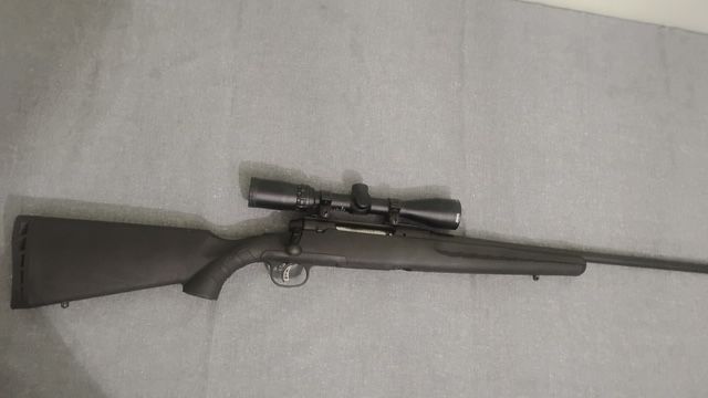 Black bolt-action rifle with scope on a light gray surface.
