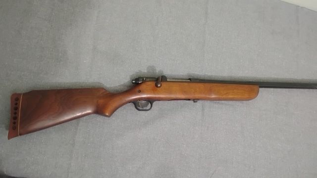 Wooden-stock rifle lying on a gray fabric surface.