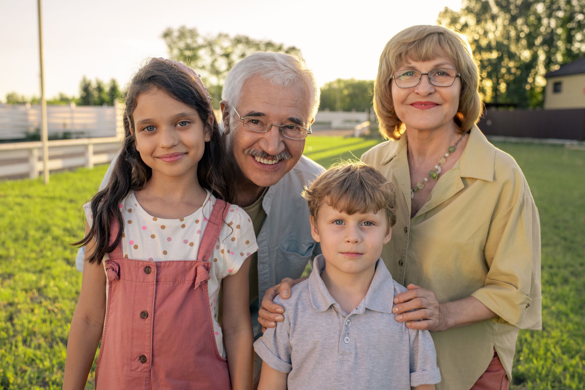 Grandparents with two grandchildren smile for a photo outdoors.