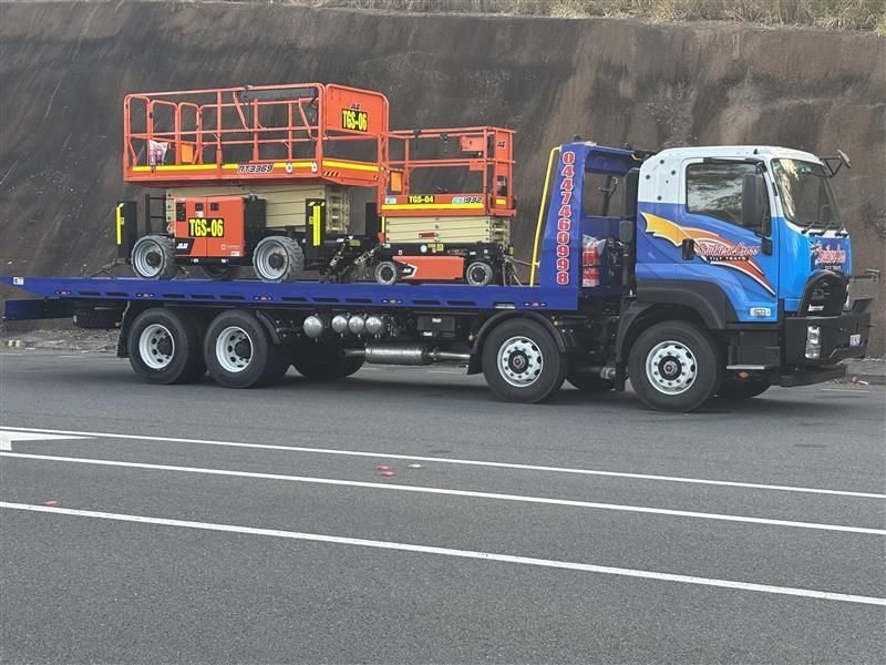 Blue flatbed truck carrying orange cherry picker on a roadway — Southern Cross Tilt Trays in Townsville, QLD