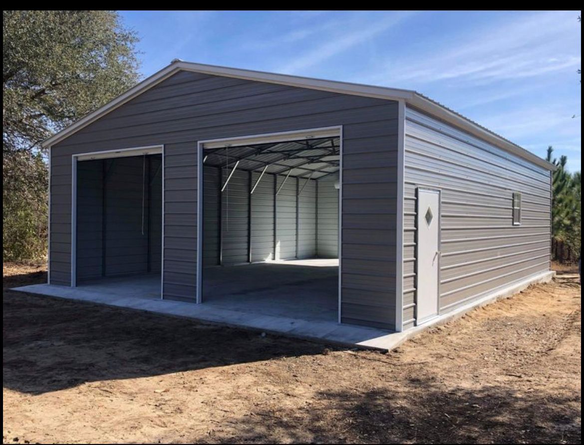 Gray metal storage building with open garage-style doors on a dirt lot
