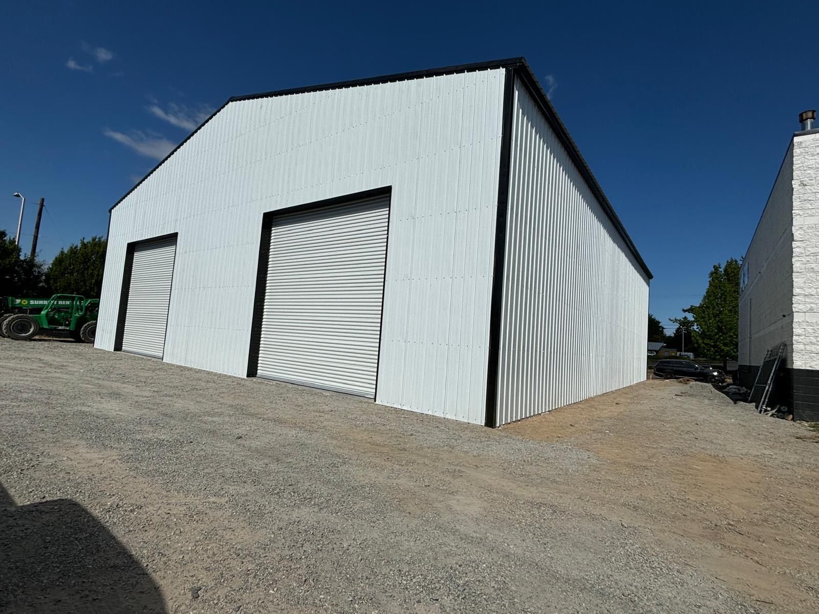 White metal storage building with roll-up doors on a gravel lot under a blue sky