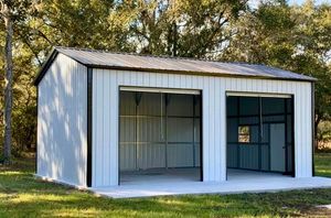 White metal garage-style shed with two open bays in a grassy yard, backed by trees