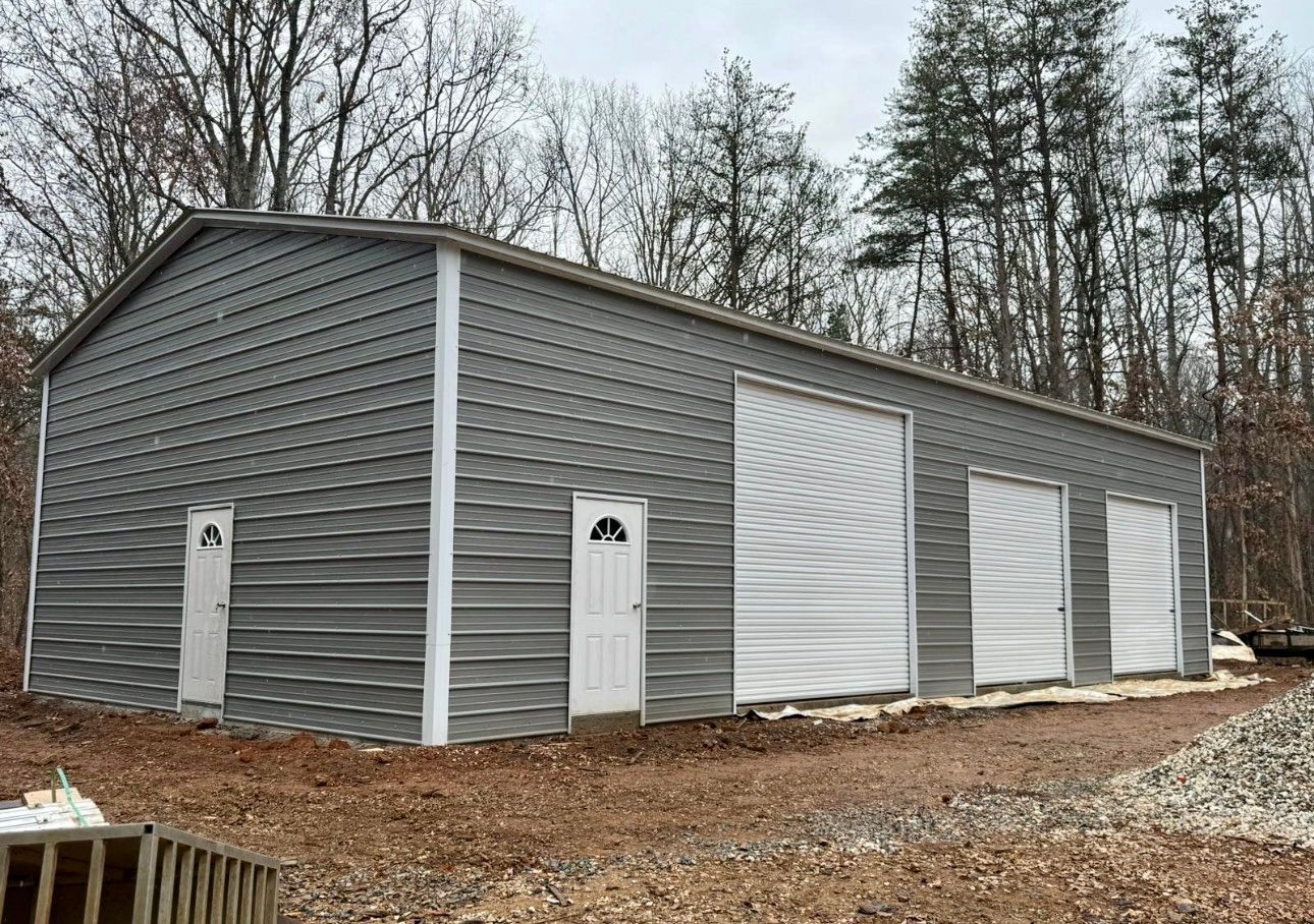 Gray metal storage building with white roll-up doors in a wooded area