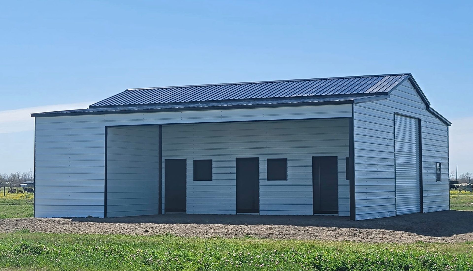 Small blue-gray metal building with a blue roof, set in a grassy field under a clear sky