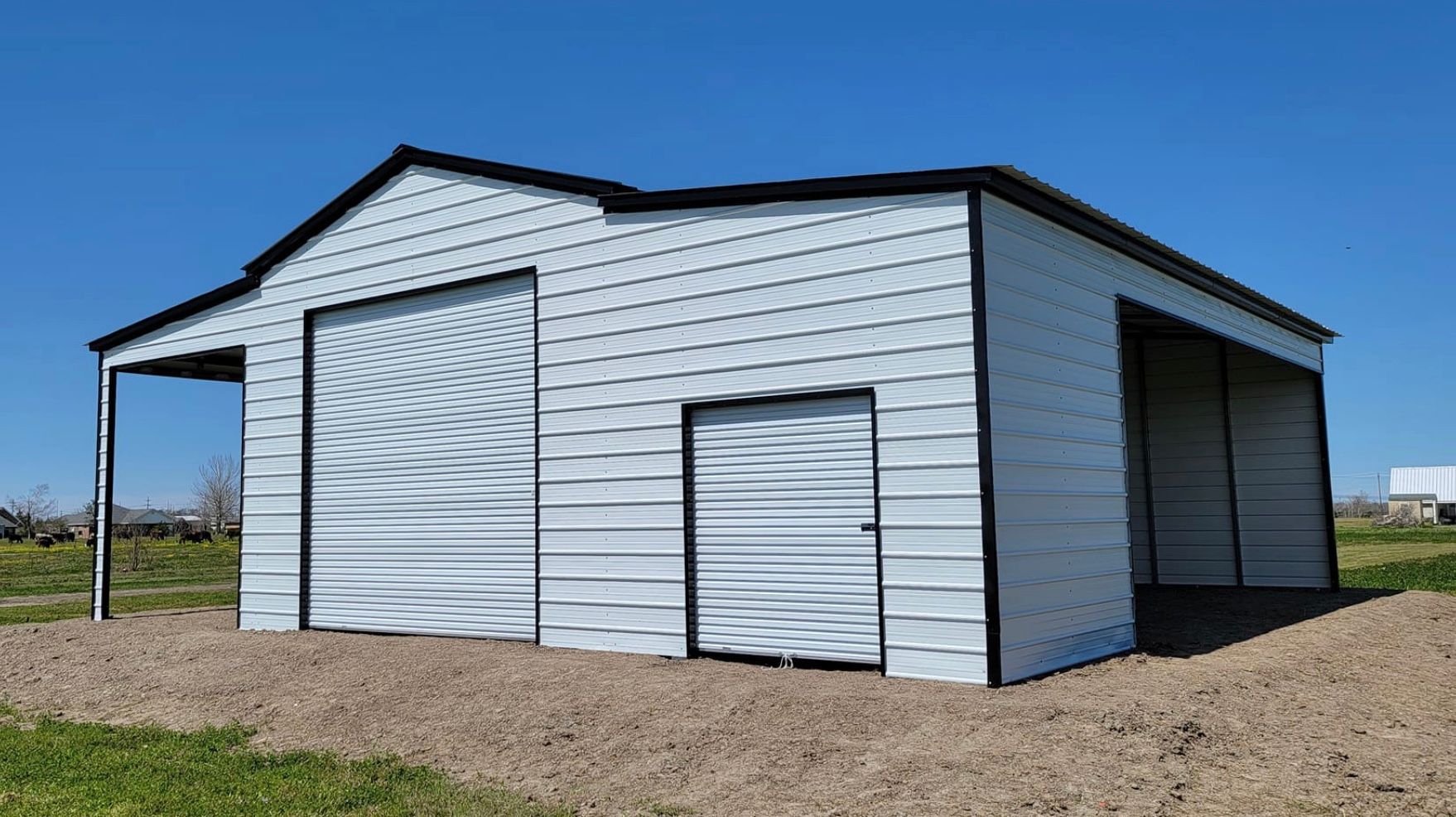 White metal storage shed with large garage door and side door, standing on a gravel lot under a blue sky