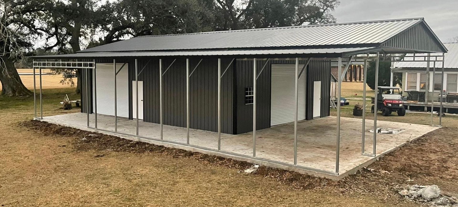 Small corrugated metal shed with open porch, on concrete slab in a rural yard.