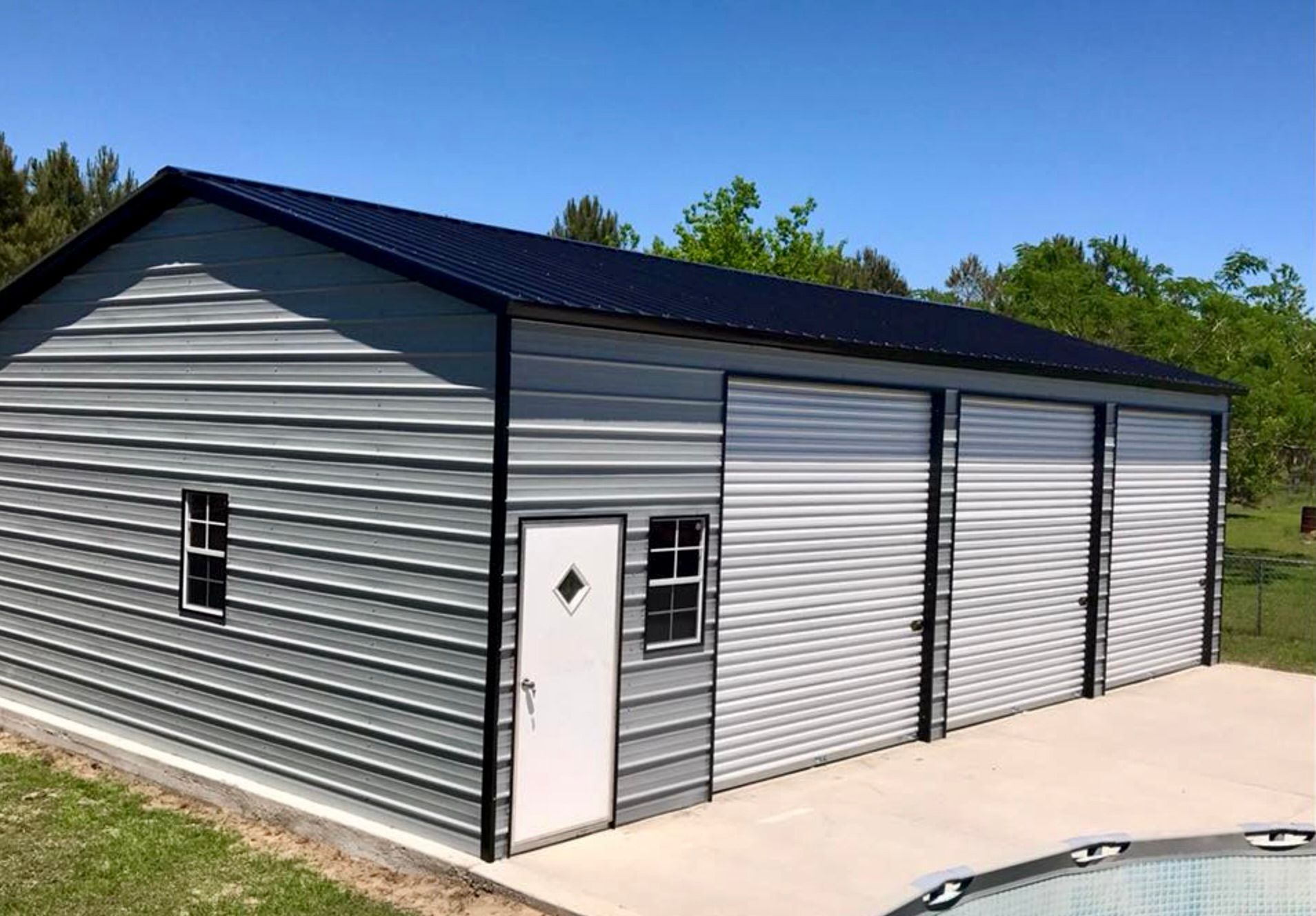 Gray metal garage with a white side door and two roll-up doors on a concrete driveway