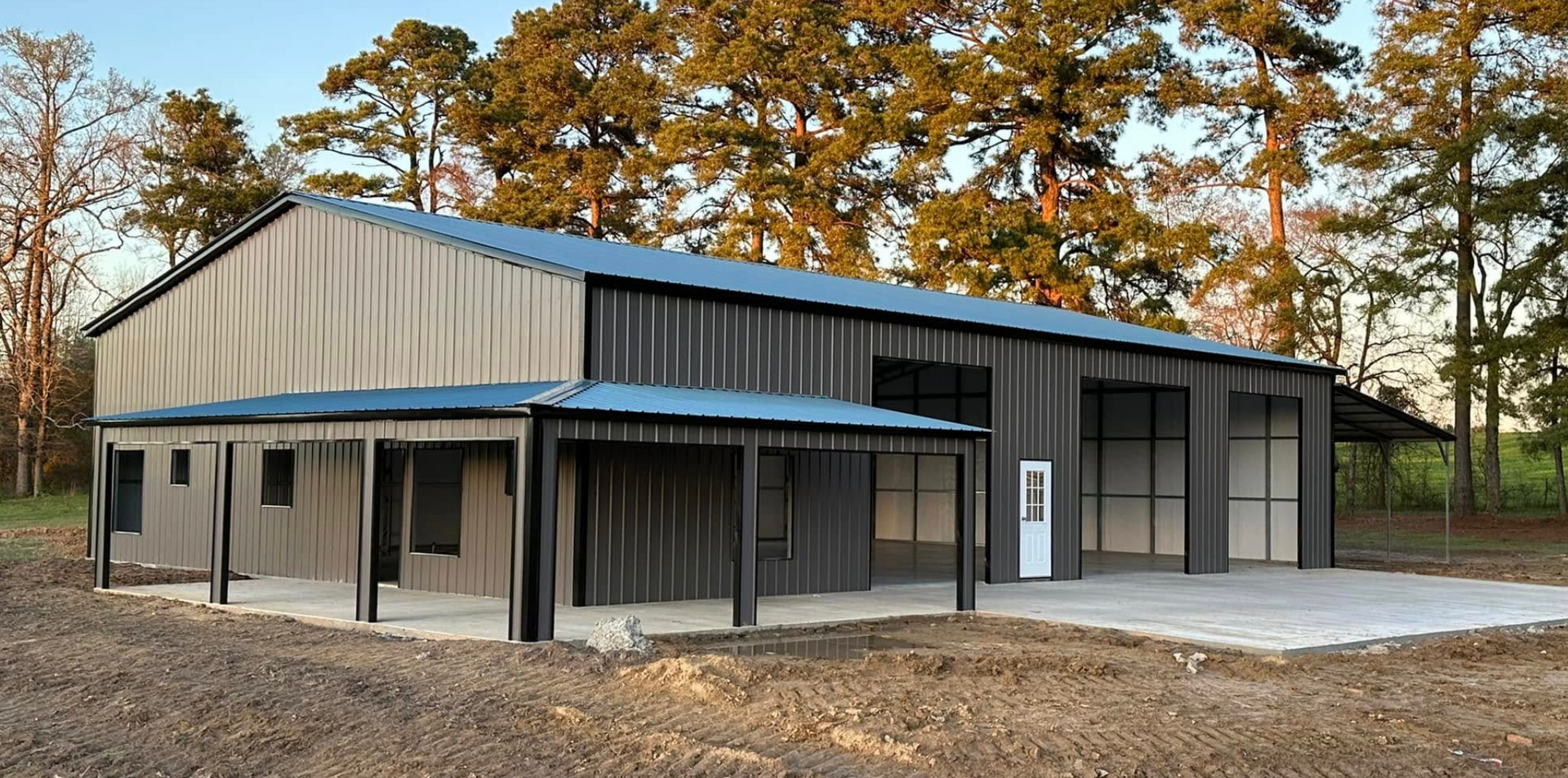 Modern metal building with a covered porch, gray siding, and large windows amid autumn trees