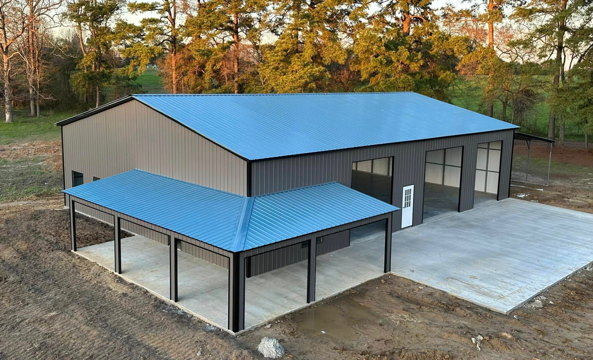 Modern gray building with blue metal roofs and a covered parking area in a wooded setting