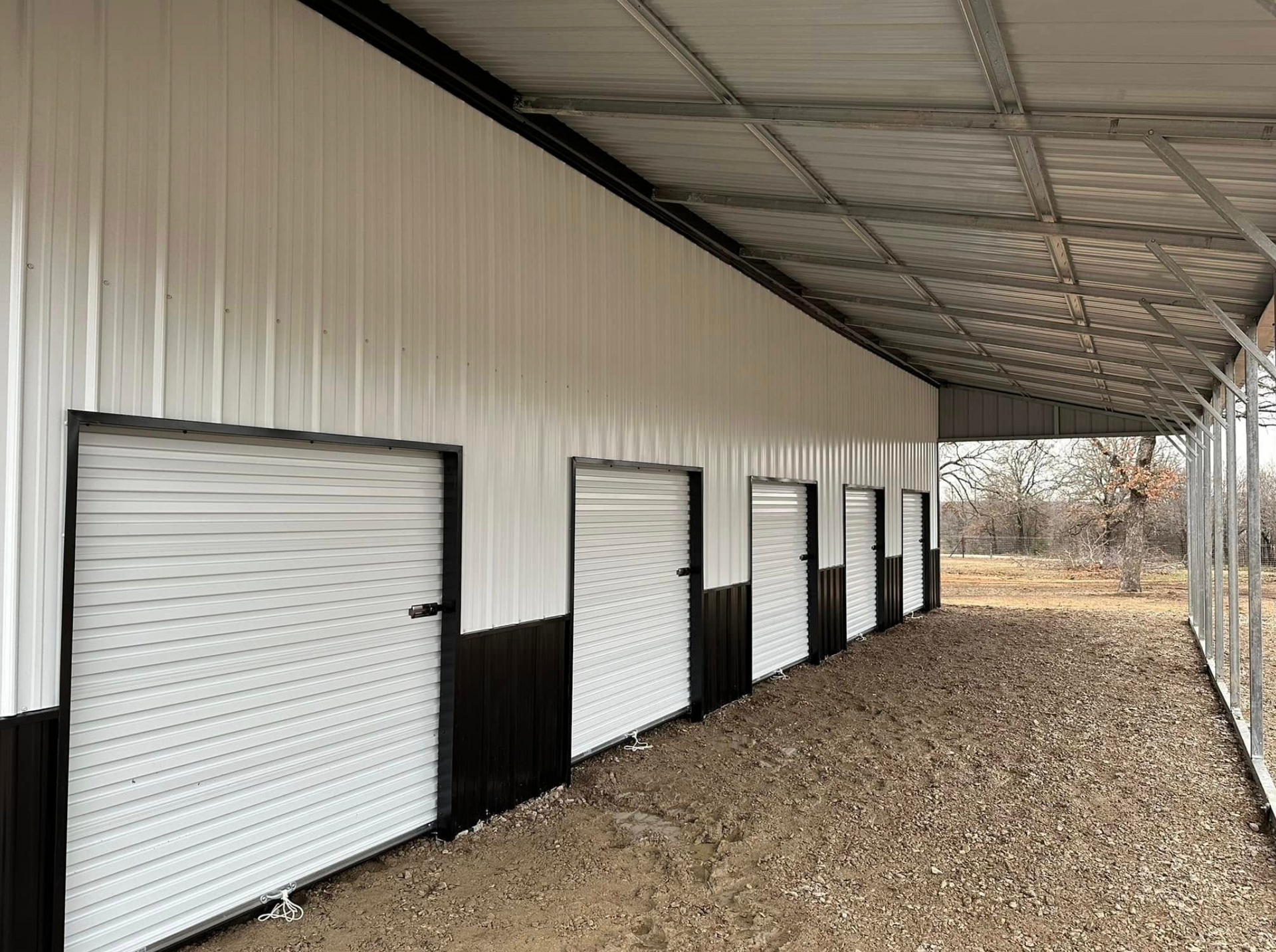 Row of white storage unit doors along a covered gravel corridor with black lower walls