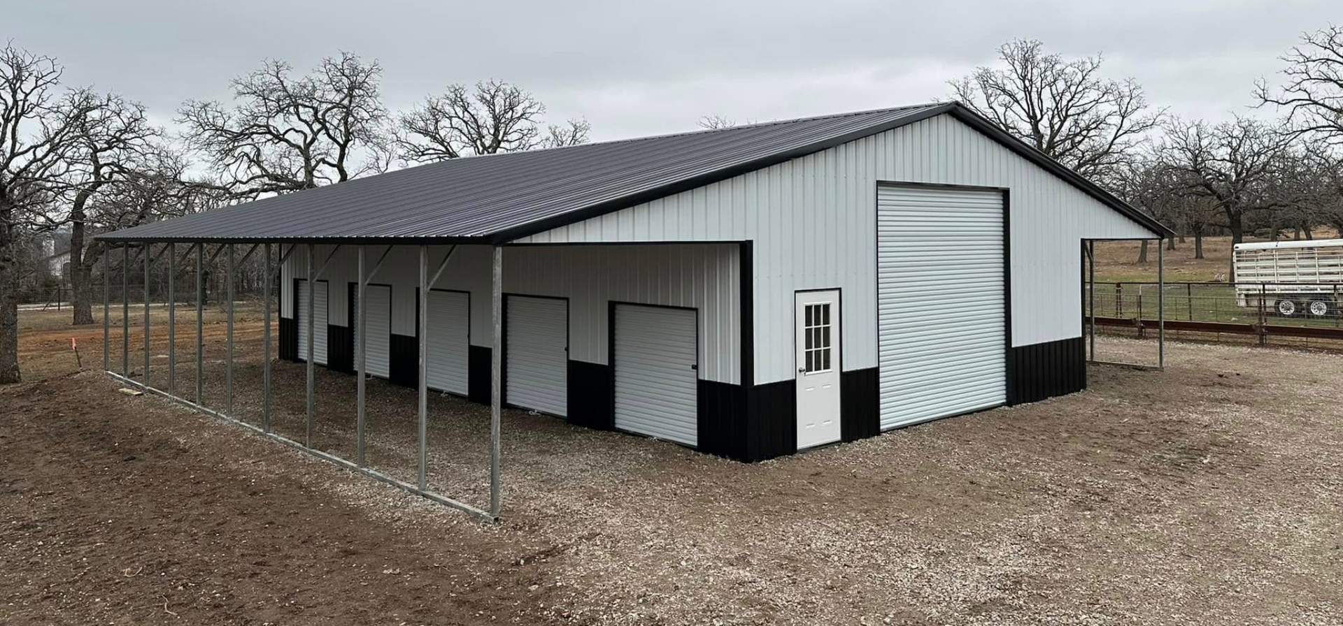 White and black metal barn or stable with open stalls in a rural, leafless field