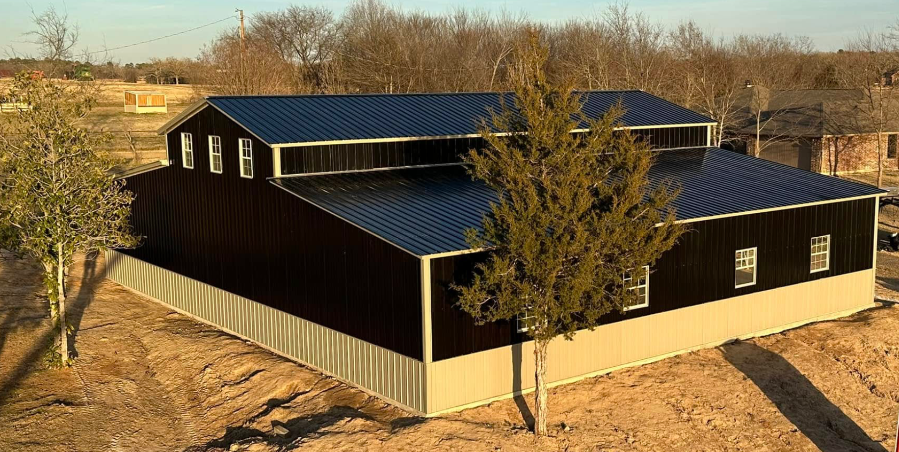 Large black barn with solar panels in a rural field, surrounded by trees