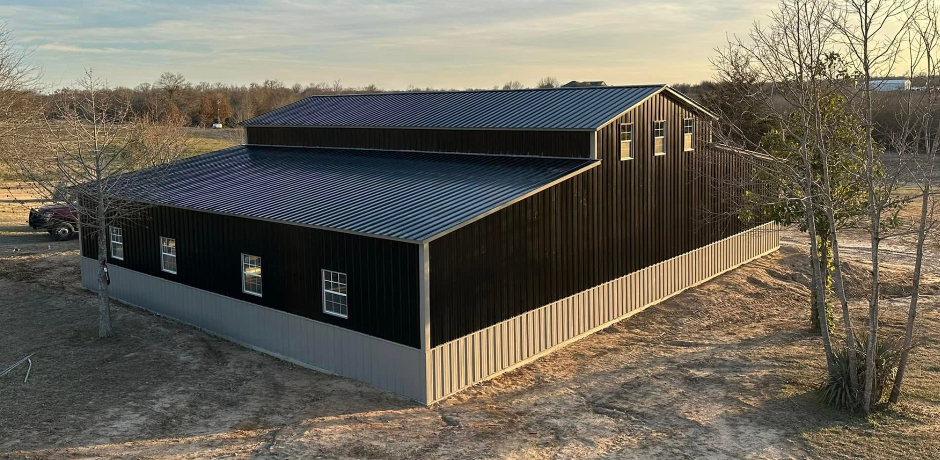 Black metal barn-like building with a corrugated roof on a wooded hillside at sunset