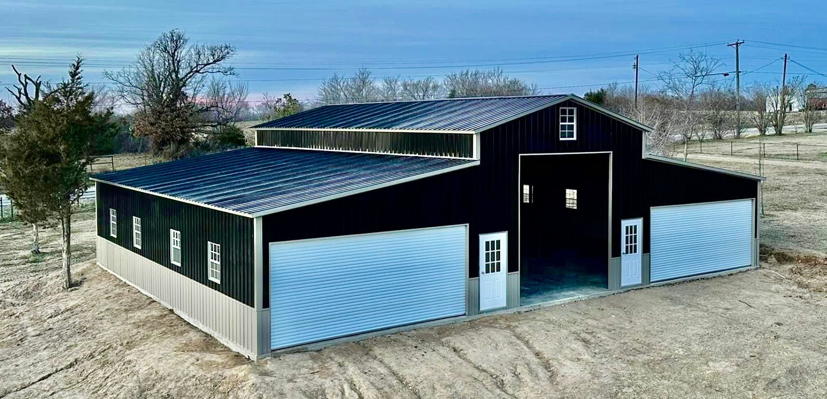 Black barn-style building with white lower walls and a dark roof in a rural field