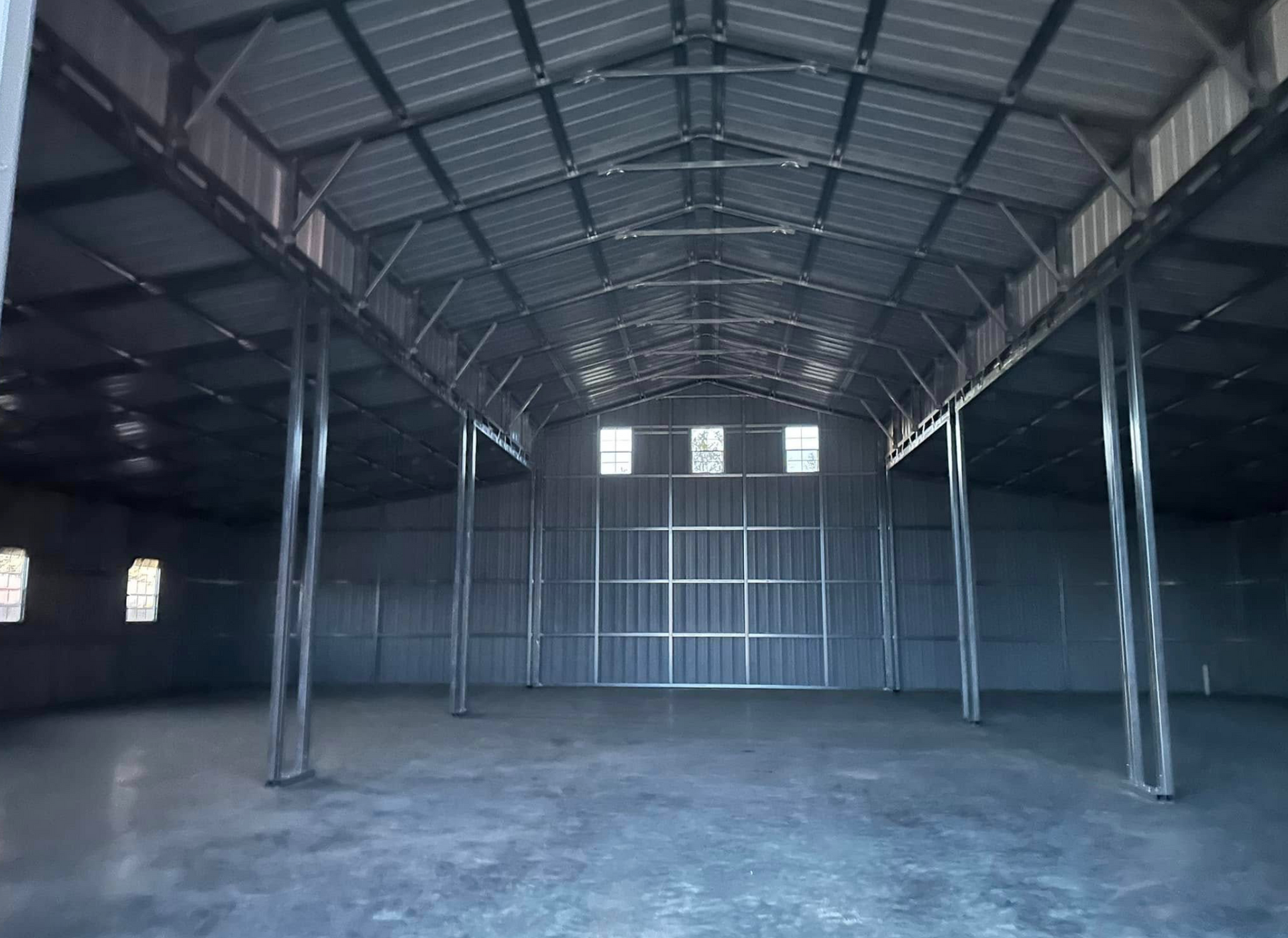 Empty metal warehouse interior with high arched roof and concrete floor