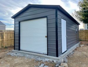 Gray detached garage with roll-up door and side entry door in a fenced yard