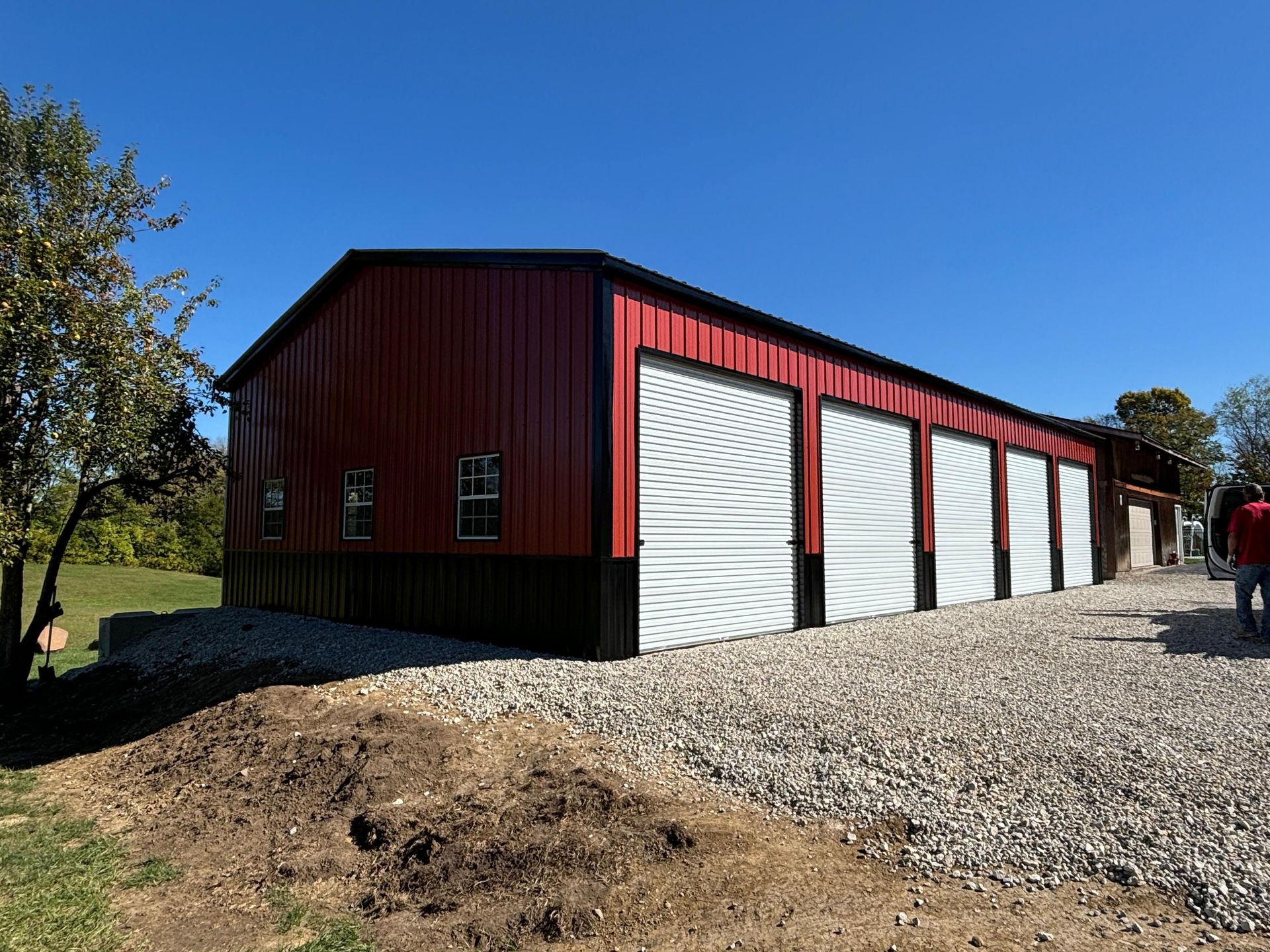 Red metal barn with white doors on a gravel lot under a clear blue sky.