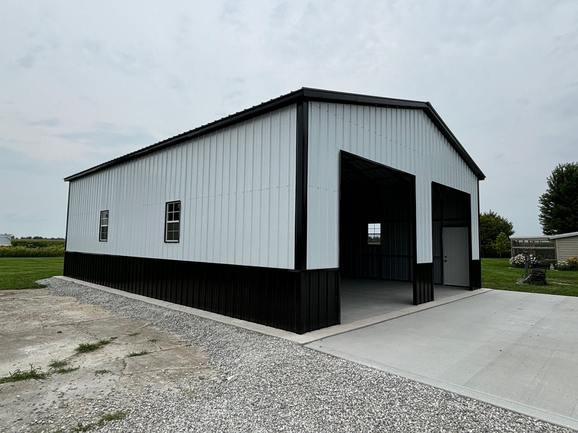 White and black metal barn-style building with open garage bays on a gravel lot.