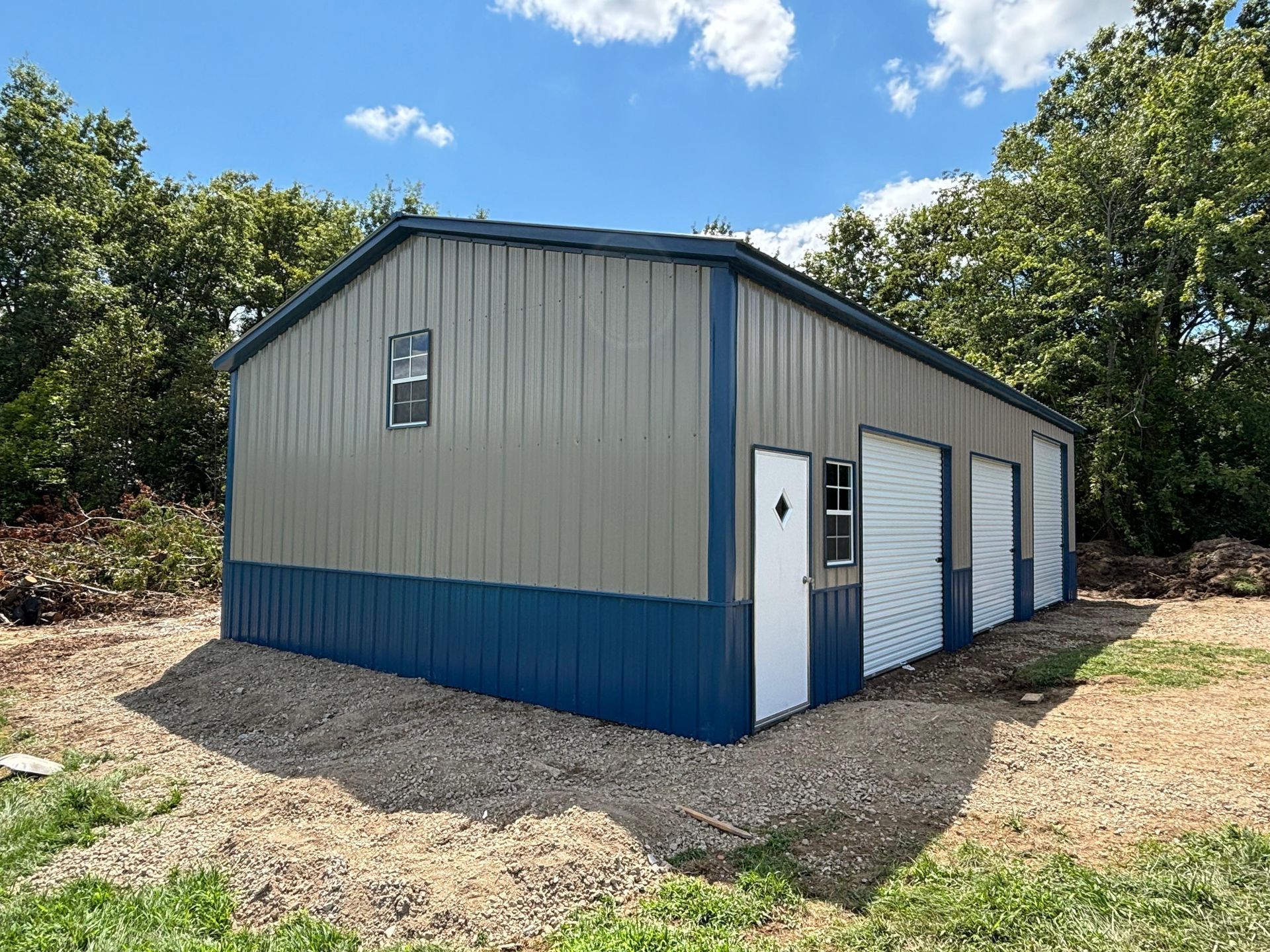 Blue-and-gray metal storage building with white doors on a gravel lot under a sunny sky