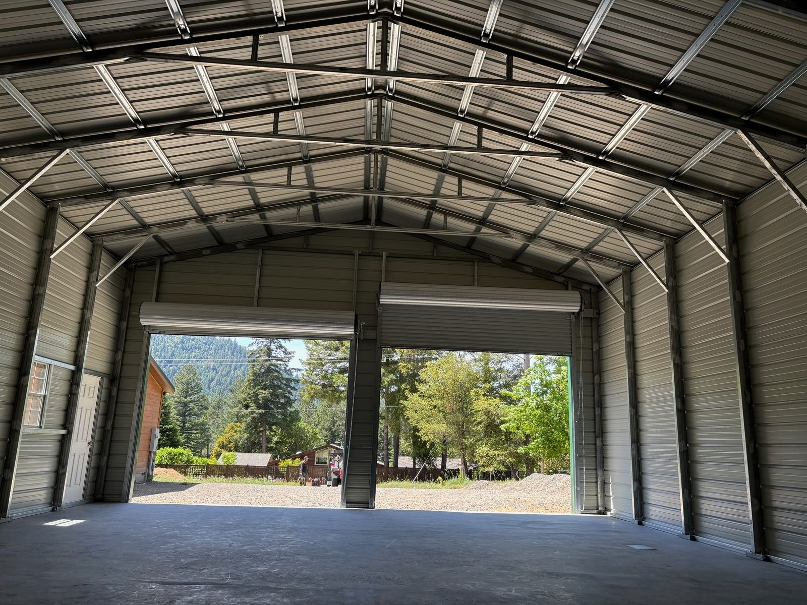 Gray metal storage shed with open front doors, showing a spacious interior on a dirt lot.