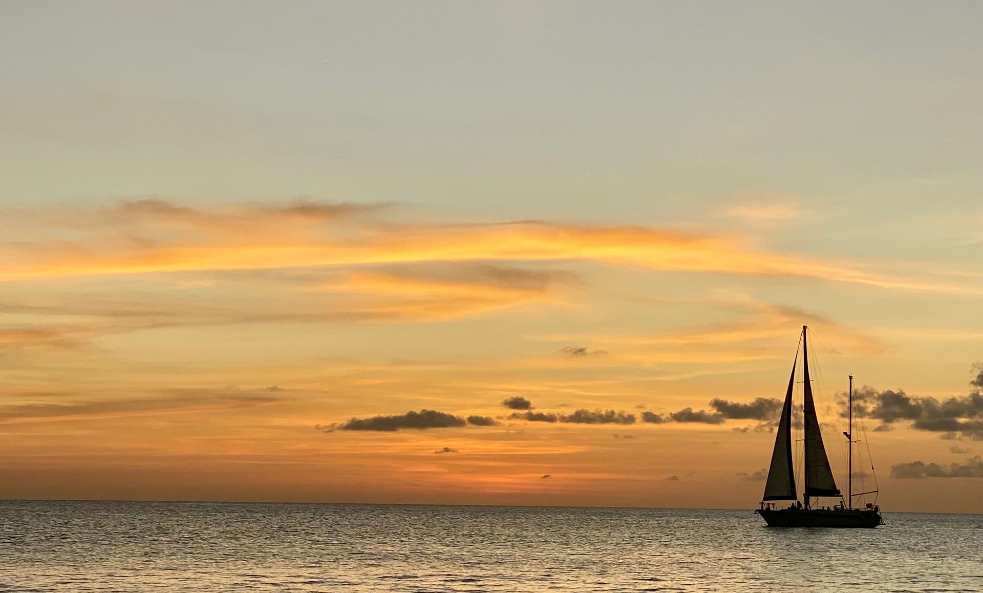 Blue Bay Bonaire Sunset Sail, a sailboat cruises on the sea before a golden sunset.