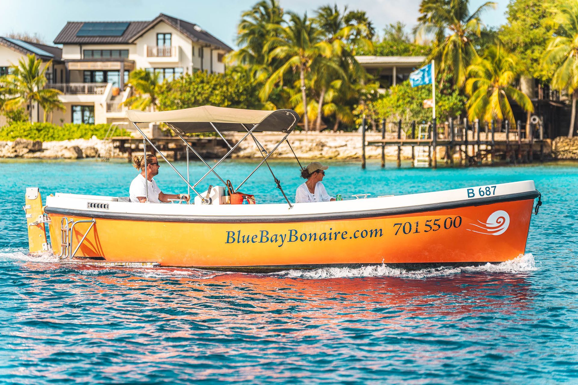Blue Bay Bonaire orange Sloop rental motor boat cruising along the coastline of Bonaire.