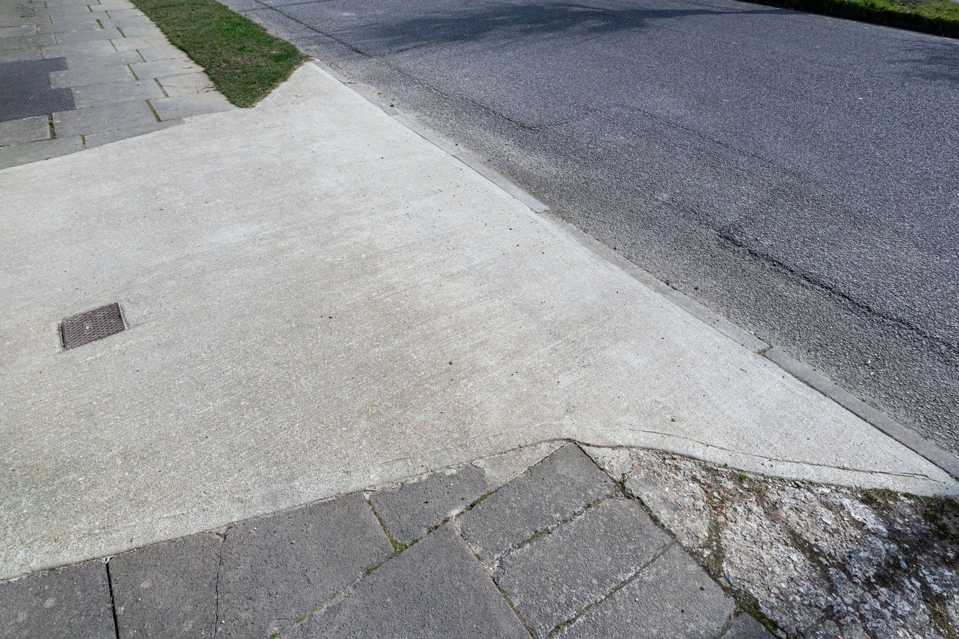 A paved concrete driveway ramp transitioning smoothly from a stone walkway to a dark asphalt street.