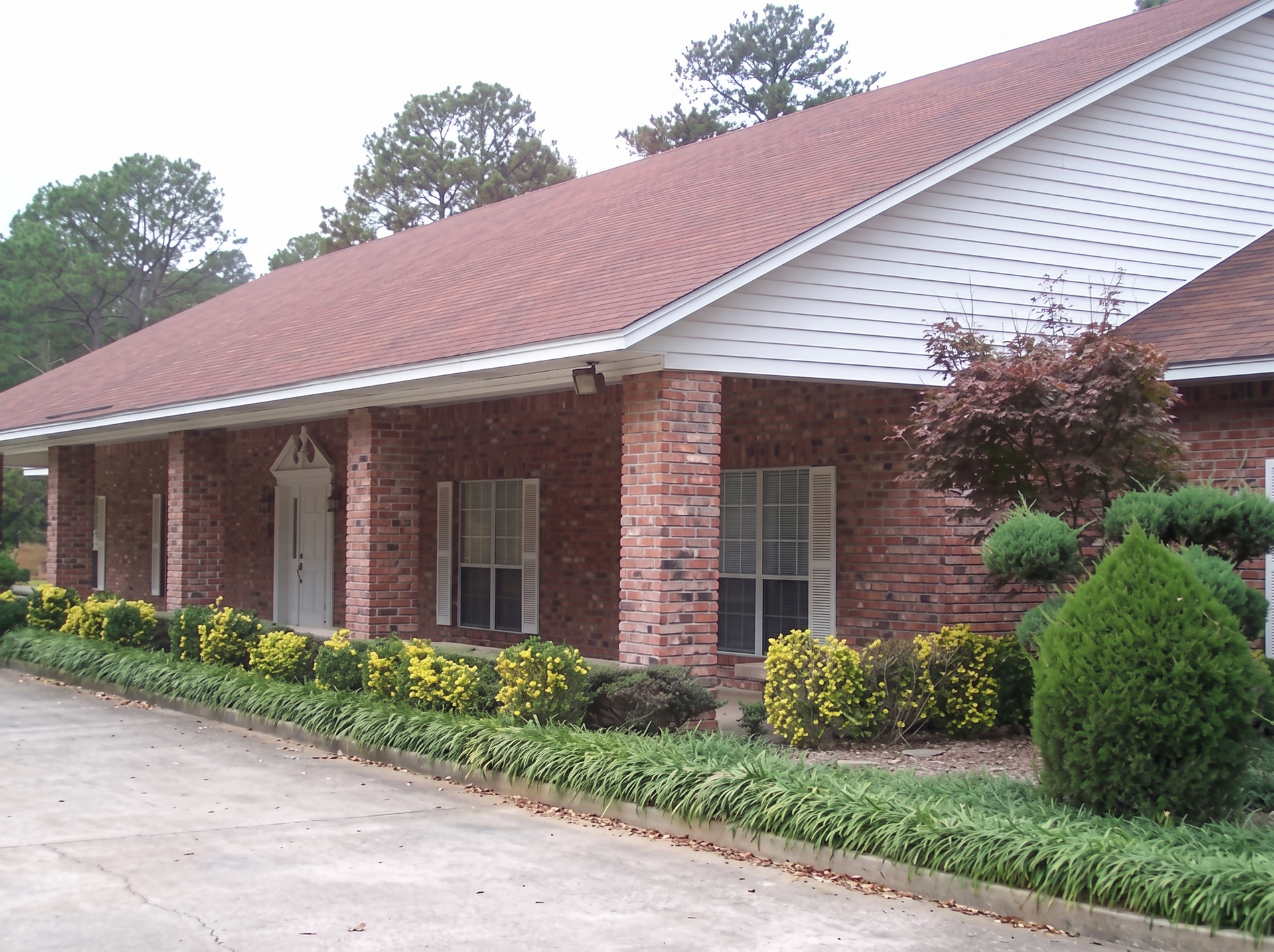 Brick building with red roof, white trim, and flower beds along a driveway