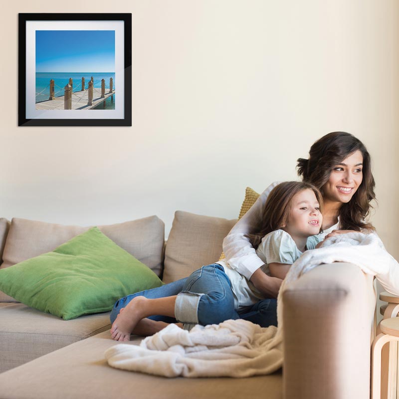 A woman and child are sitting on a couch with a picture on the wall above them. mini-split 