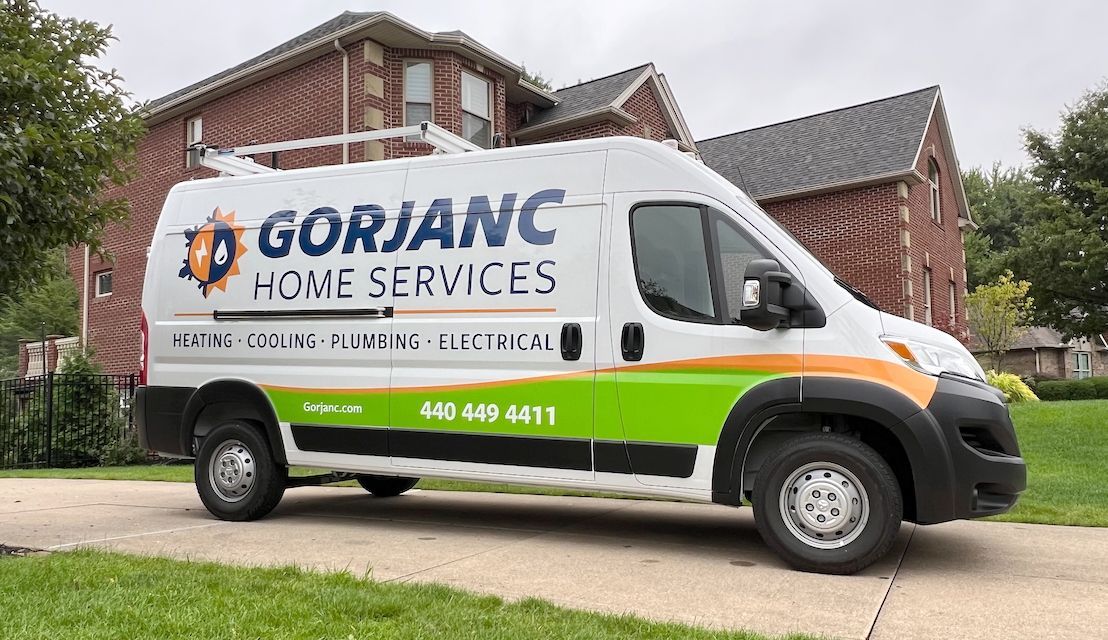 A white Gorjanc Home Services van with green and orange accents parked in a driveway in front of a brick house.