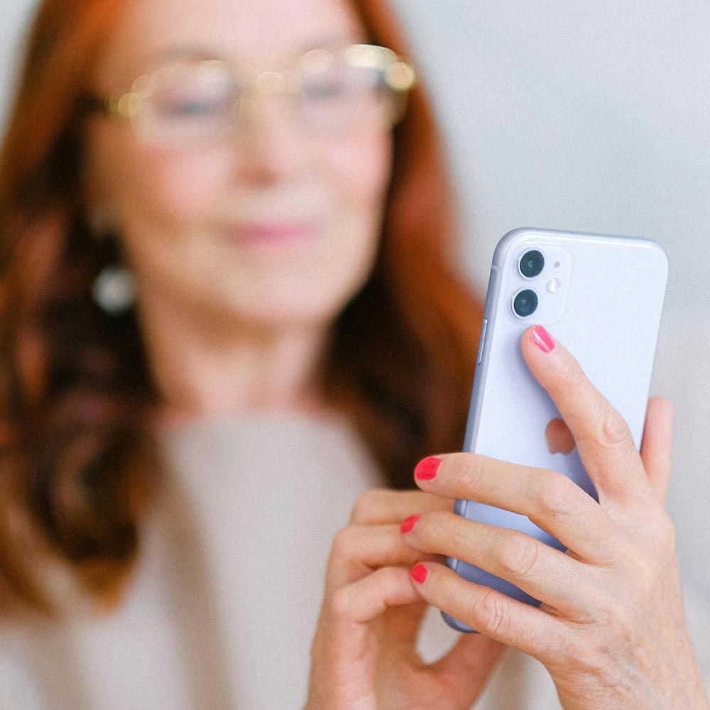 A person with red hair and glasses holds a light purple smartphone, focused on the screen.