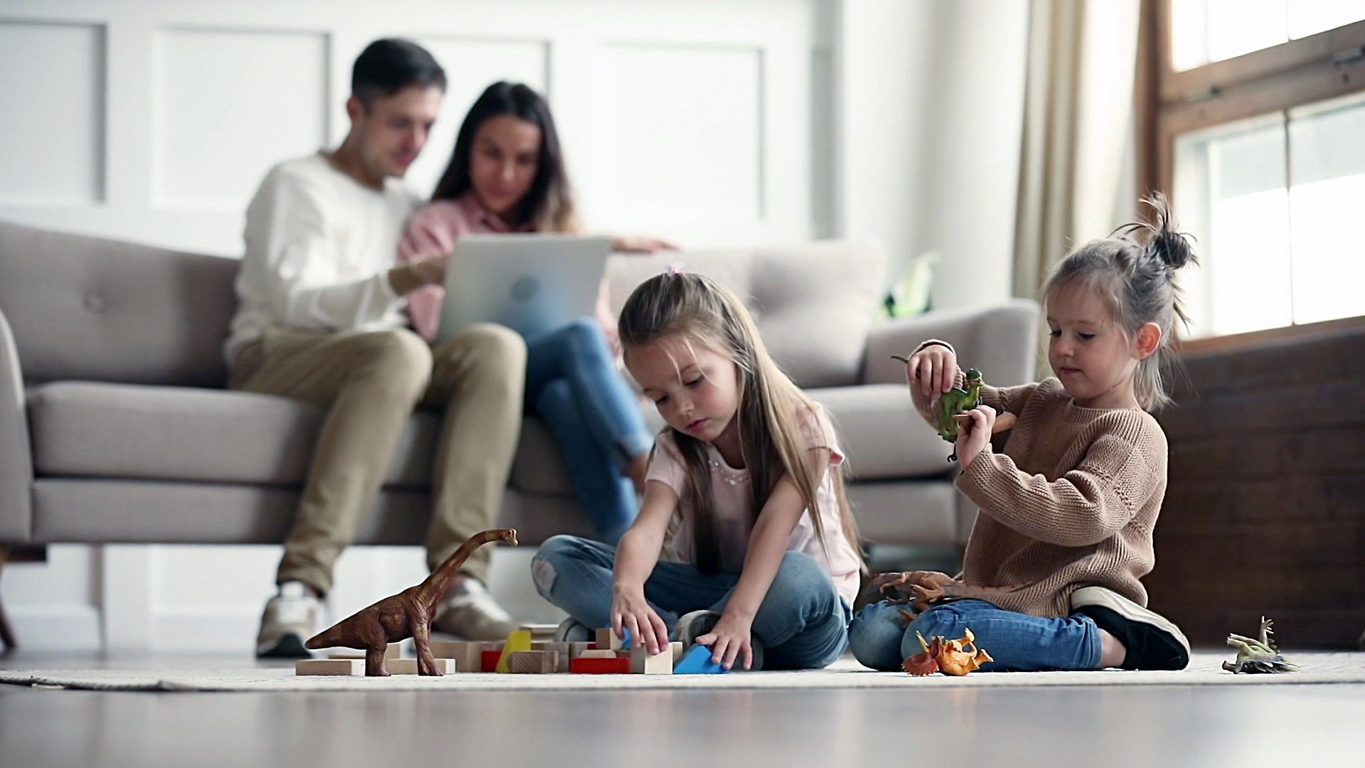 A family is sitting on a couch playing with toys and a laptop.